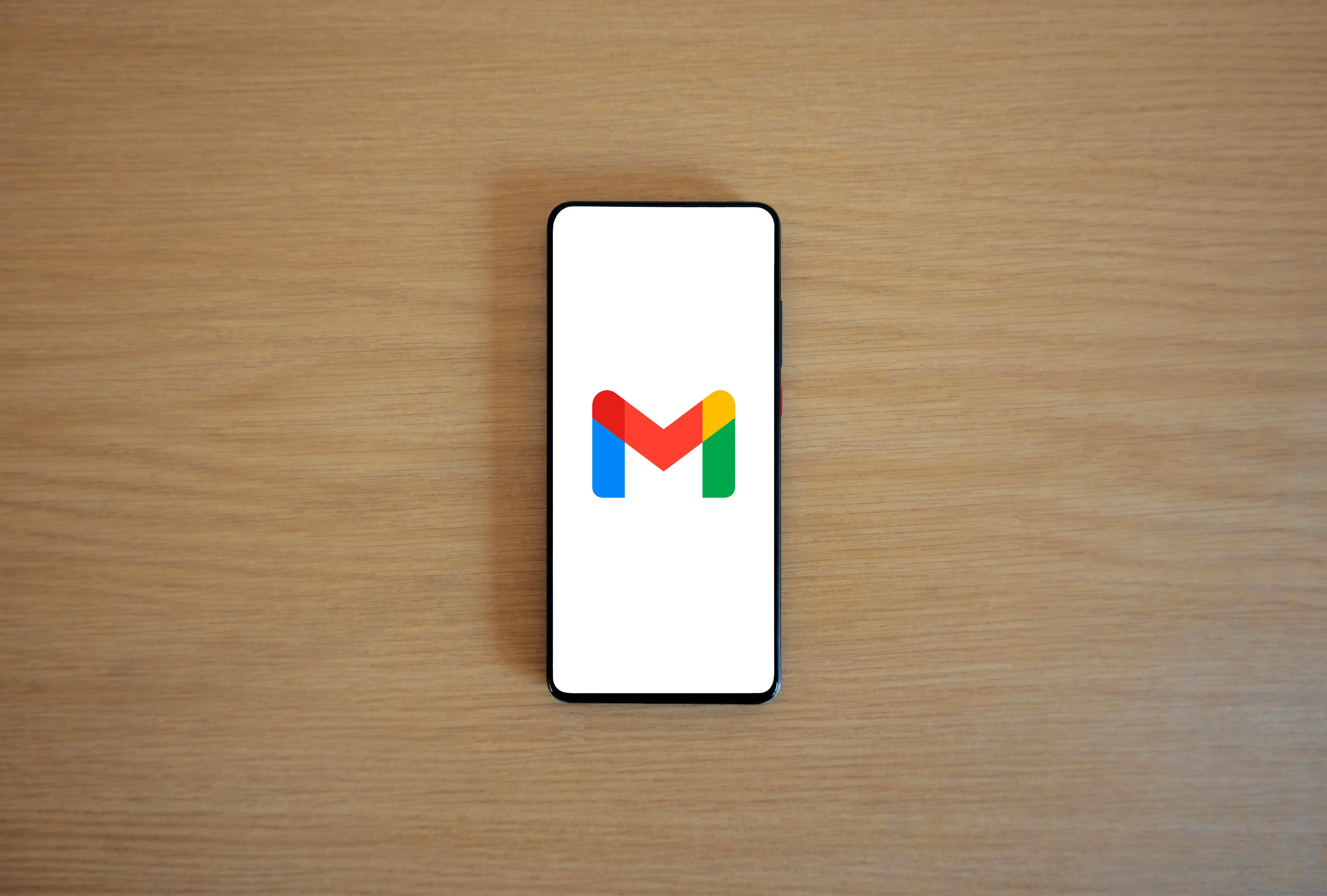 Mobile with Gmail logo on center of its screen kept on a table